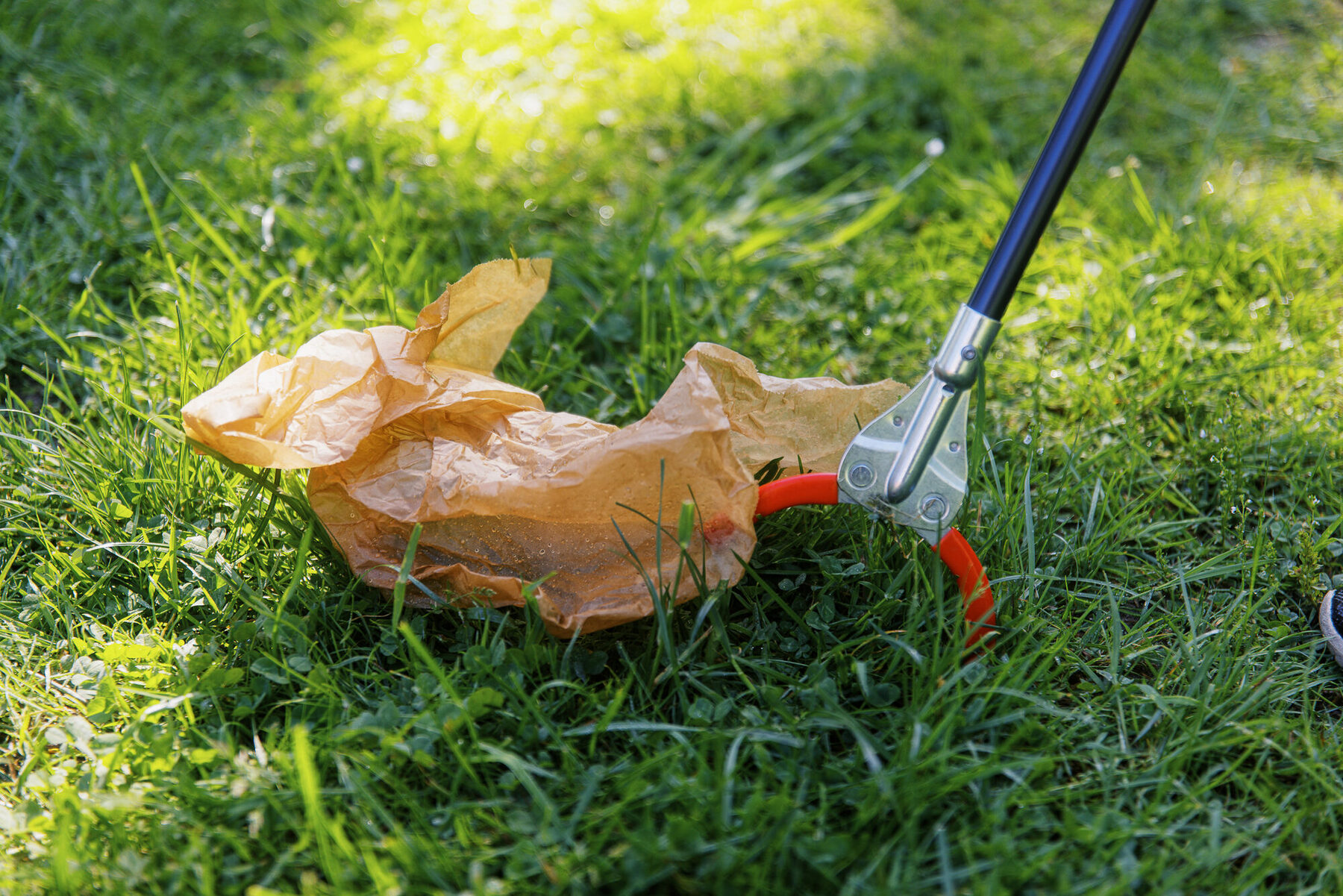 Ein Müllgreifer hebt eine Papiertüte aus dem Gras